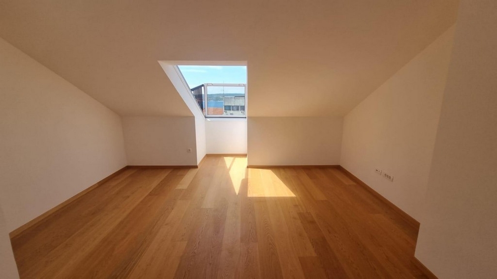 Světlá ložnice se střešním oknem.