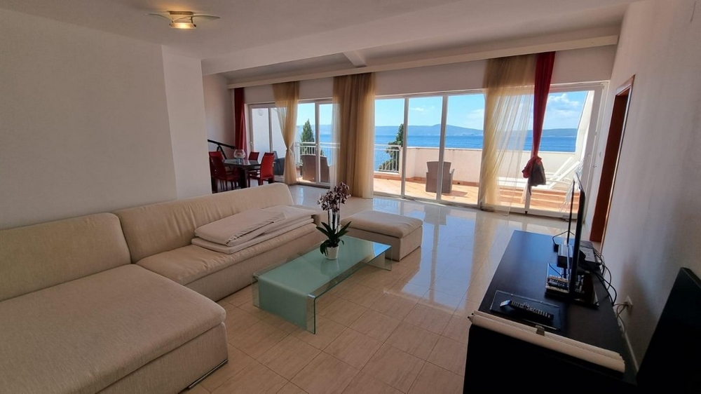 Světlý obývací prostor s krémovým gaučem a moderní dlažbou. Skvělý výhled na moře.