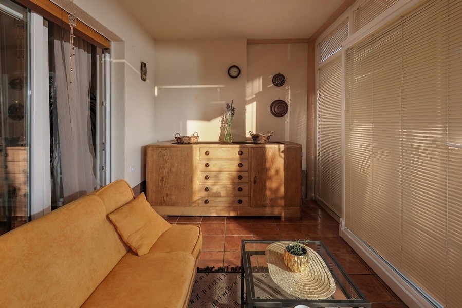 Sluncem zalitá zimní zahrada chorvatského bytu se žlutou pohovkou.