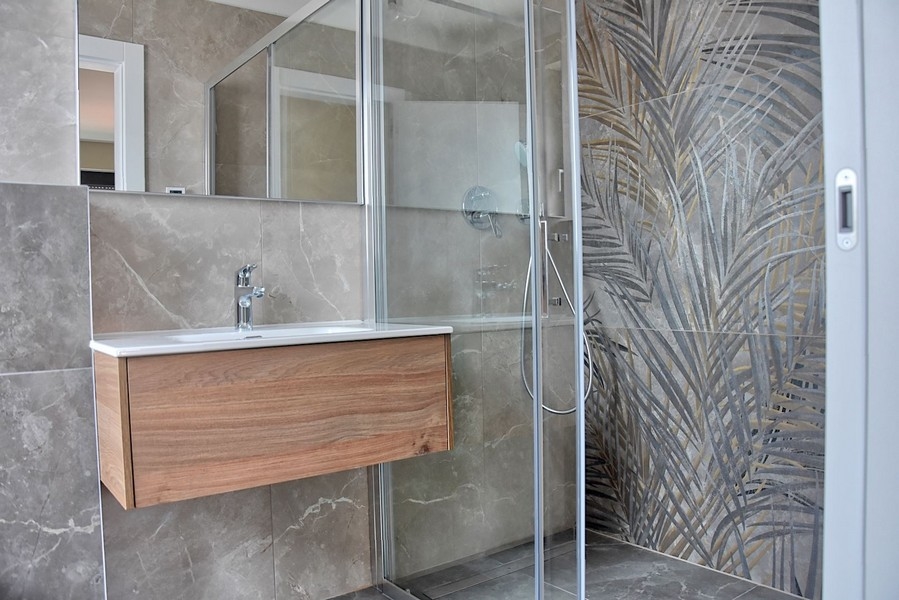 Moderní koupelna v penthouse na Istrii se sprchovým koutem s dekorativním skleněným obkladem a dřevěným umyvadlem.