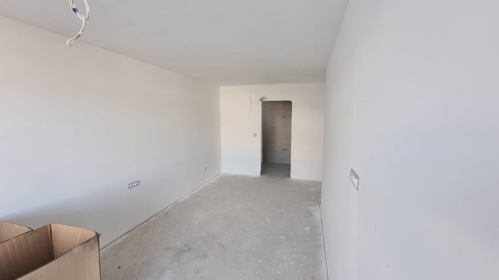 Prázdná místnost bytu v Chorvatsku se světlými stěnami a betonovou podlahou.