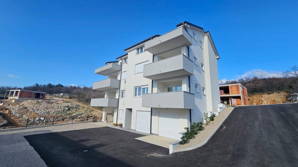 Vnější pohled na bílý bytový dům na prodej v Crikvenici, Chorvatsko, s parkovacím místem a jasnou modrou oblohou