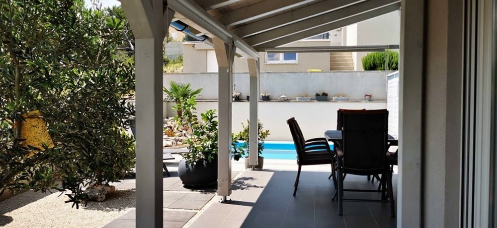 Krytá terasa s venkovním jídelním koutem, část bytu na prodej v Tisnu, Chorvatsko, s výhledem na bazén.