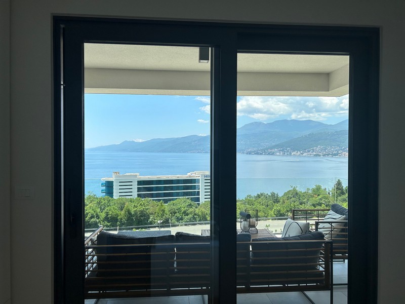 Pohled přes otevřené dveře na terasu moderního bytu s výhledem na Kvarnerský záliv.