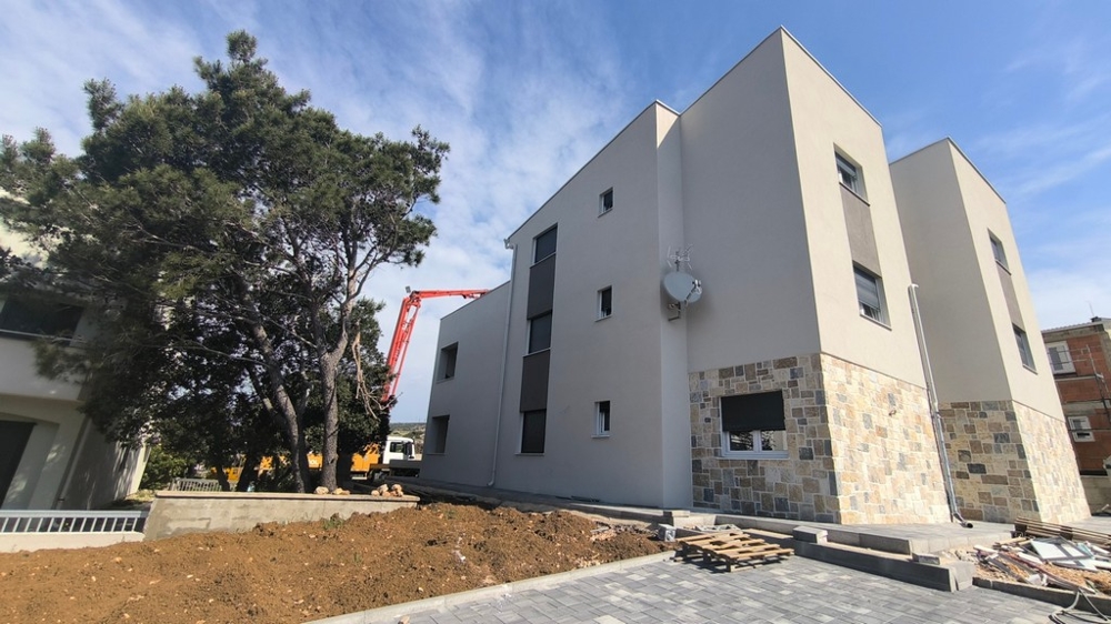 Novostavba moderního penthouse, nemovitost v Chorvatsku v Šimuni s venkovními parkovacími místy a stromem v popředí.