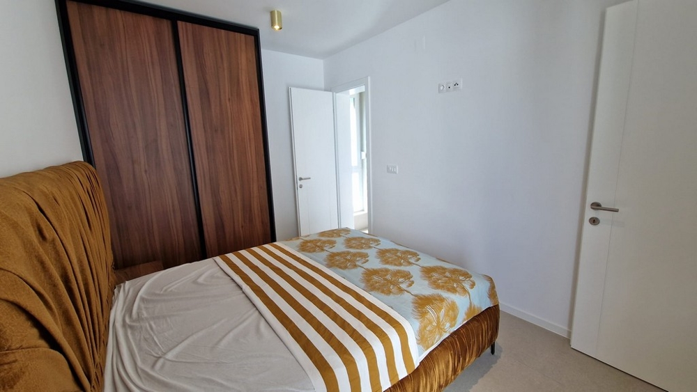 Ložnice apartmánu v Novalji na ostrově Pag, s pruhovaným ložním prádlem a dřevěnými prvky, chorvatská nemovitost