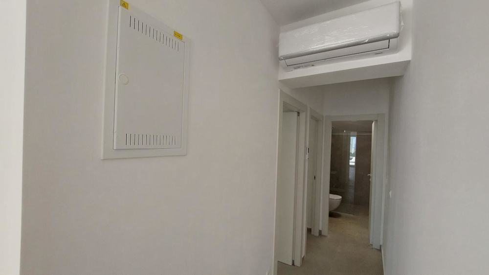 Vnitřní pohled na prázdnou místnost s dlážděnou podlahou, velkými okny a několika dveřmi