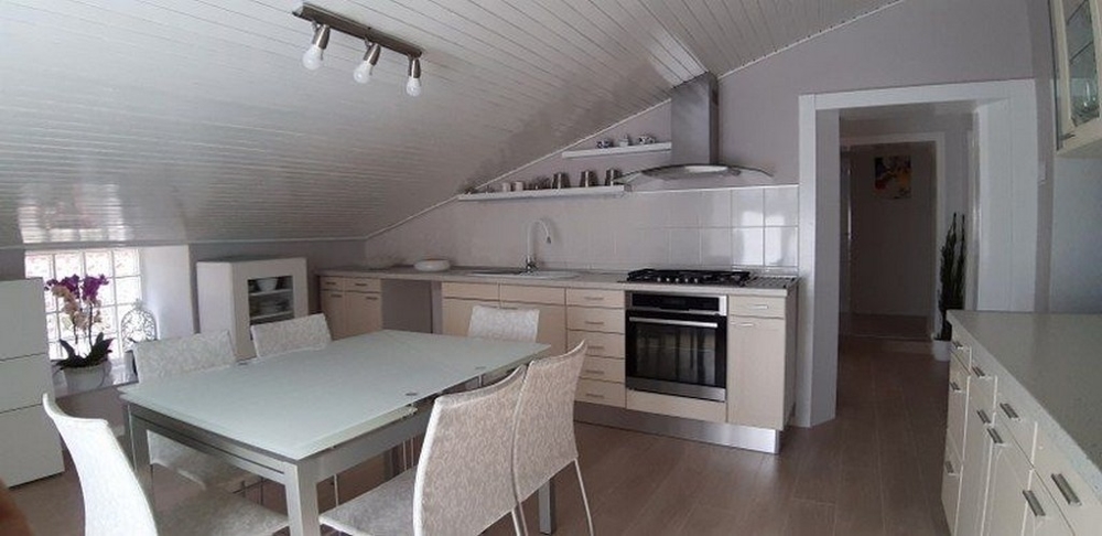 Moderní, světlá kuchyně s bílým interiérem a jídelním koutem pod šikmým stropem