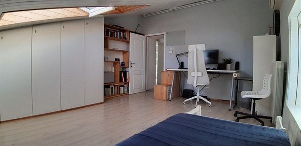 Pracovna s psacím stolem, policemi a jednolůžkem, to vše ve světlé místnosti se střešním oknem