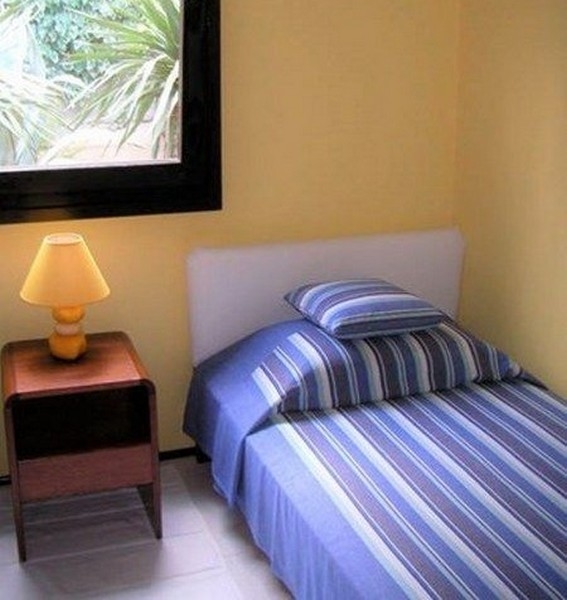 Malá ložnice se žlutými stěnami, jednolůžkem a nočním stolkem s lampou