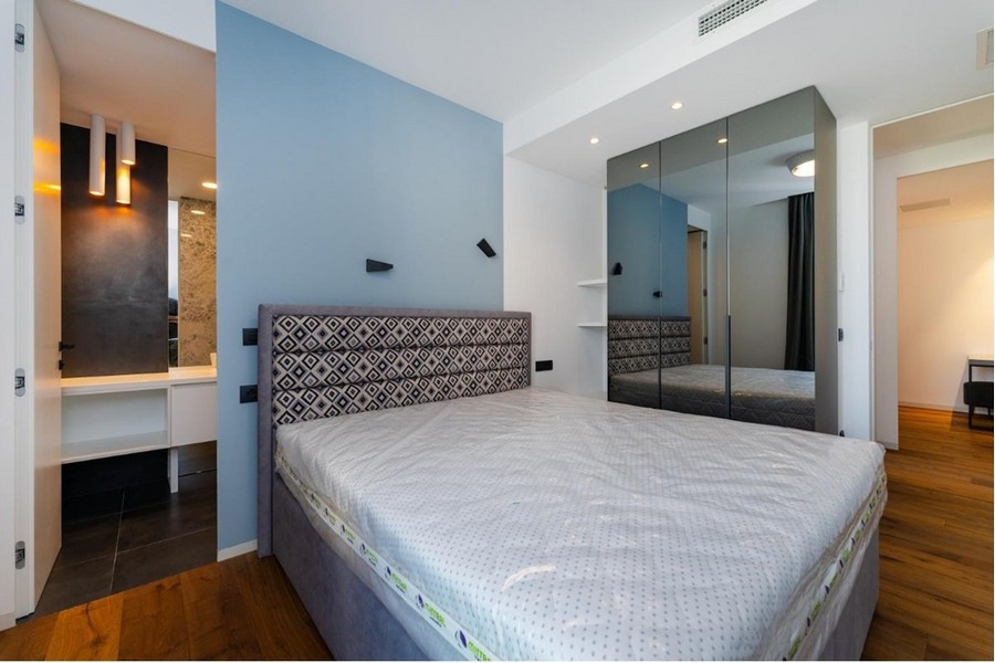 Ložnice s modrobílými stěnami, šedá postel, zrcadlová skříňka