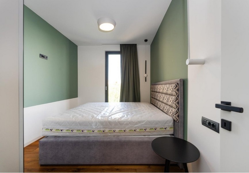 Ložnice se zelenými a bílými stěnami, šedý rám postele