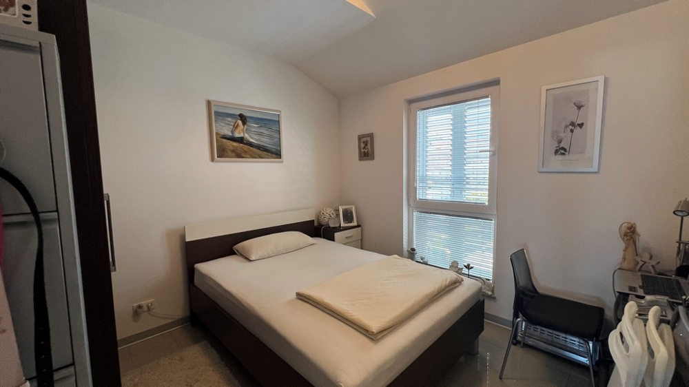 Ložnice s manželskou postelí, jednoduše zařízená s oknem do zahrady.