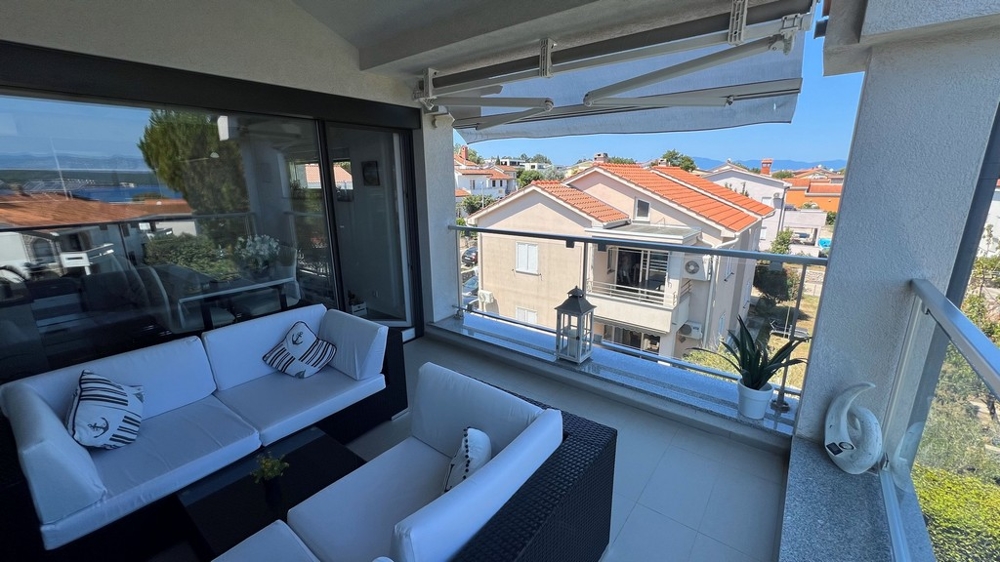 Terasa s výhledem na moře a sousední domy, zařízená bílými pohovkami a námořními polštáři.