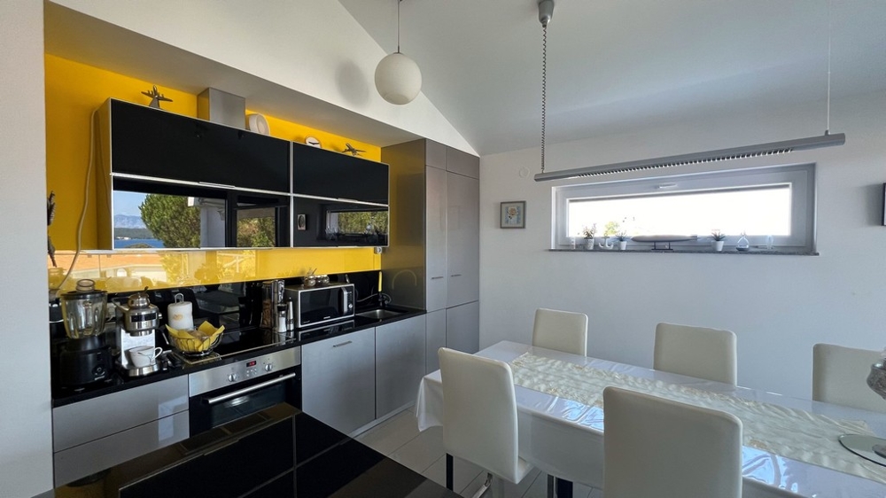 Moderní kuchyně s černou pracovní deskou a žlutou zadní stěnou, přilehlý jídelní kout.