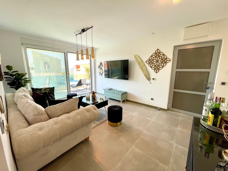 Klimatizovaný obývací pokoj se světlou pohovkou a TV.