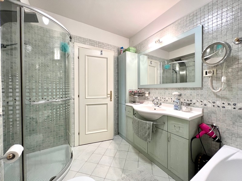 Koupelna se sprchovým koutem, velkým zrcadlem a bílými obklady