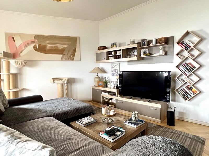Obývací pokoj s šedou pohovkou, TV s plochou obrazovkou a ozdobnými policemi