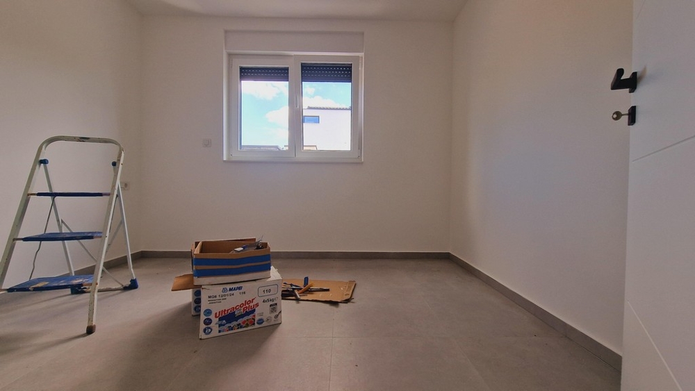 Nezařízený pokoj s šedou podlahou, žebříkem a stěhovacími boxy