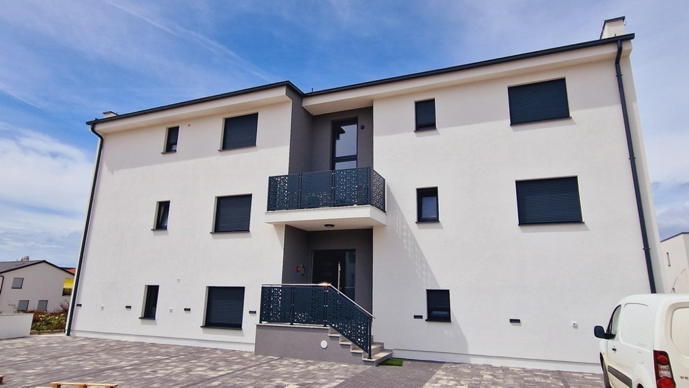 Čelní pohled na moderní budovu s bílými stěnami a balkony s kovovým zábradlím