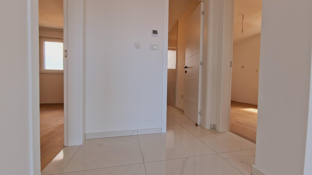 Předsíň bytu s bílými dlaždicemi a několika dveřmi do různých místností