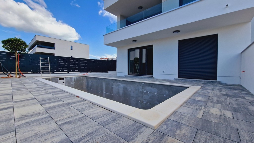 Bazén ve výstavbě před moderní budovou se skleněnými balkony a velkými terasami