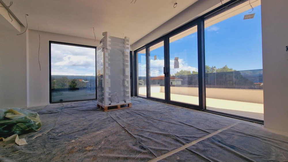 Vnitřní pohled na moderní nový apartmán s velkými okny a výhledem na terasu a moře.