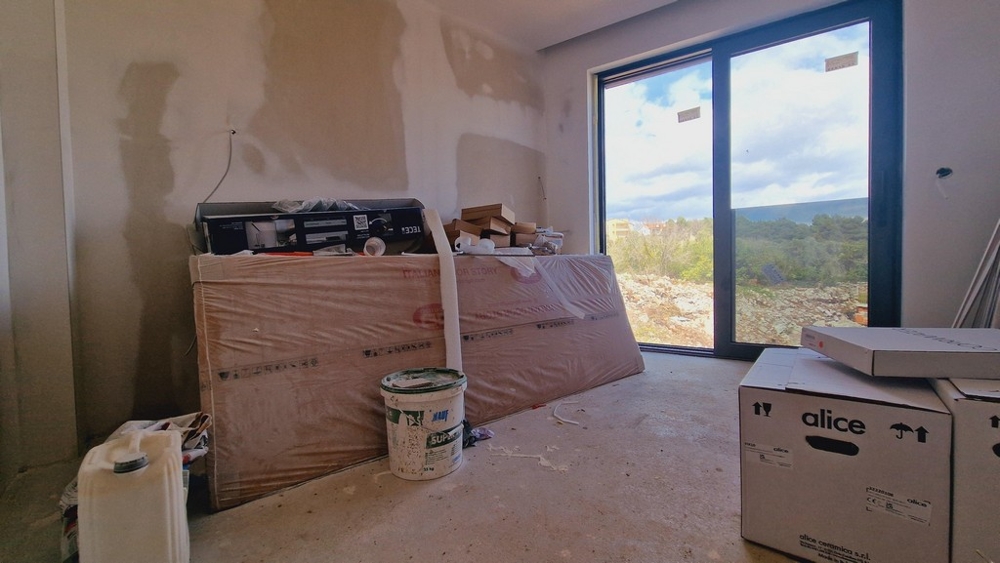 Nedokončený pokoj se staveništěm a velkým oknem s výhledem do krajiny.