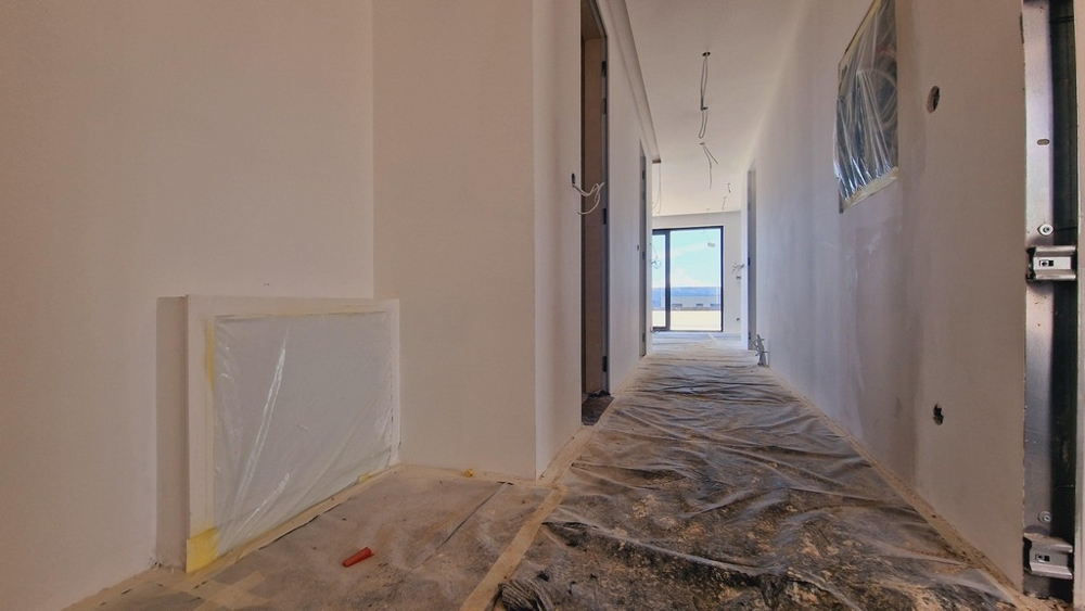 Chodba novostavby ve fázi výstavby s výhledem na terasu na konci chodby.