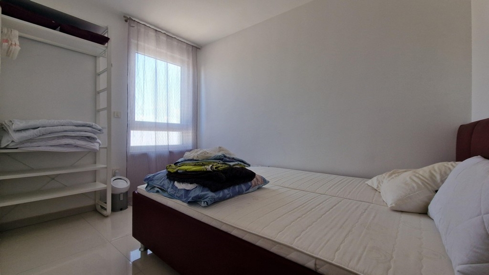 Ložnice s minimalistickým nábytkem, oknem a otevřeným úložným prostorem na oblečení.