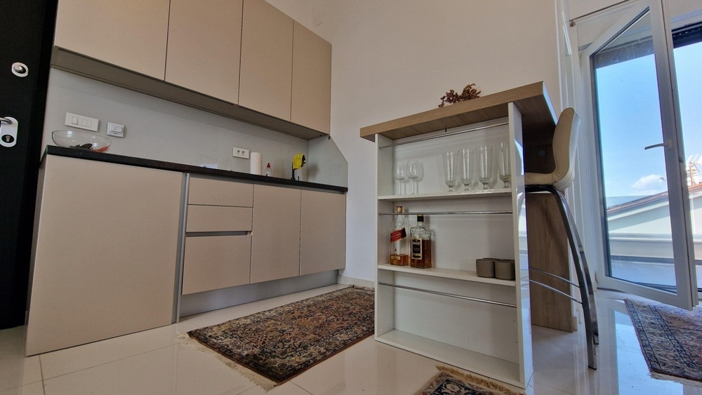 Malý, moderní kuchyňský kout s integrovanými policemi a barovými židlemi, vstup na terasu.