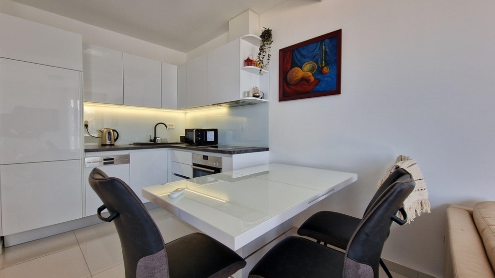 Moderní kuchyně s bílým vysoce lesklým designem, jídelním koutem a útulným nábytkem.