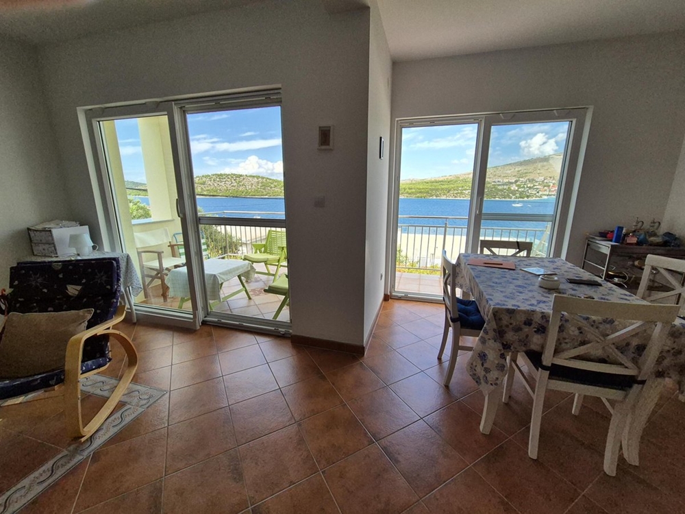 Obývací pokoj s velkým posuvným sklem, který se otevírá na terasu s výhledem na moře.