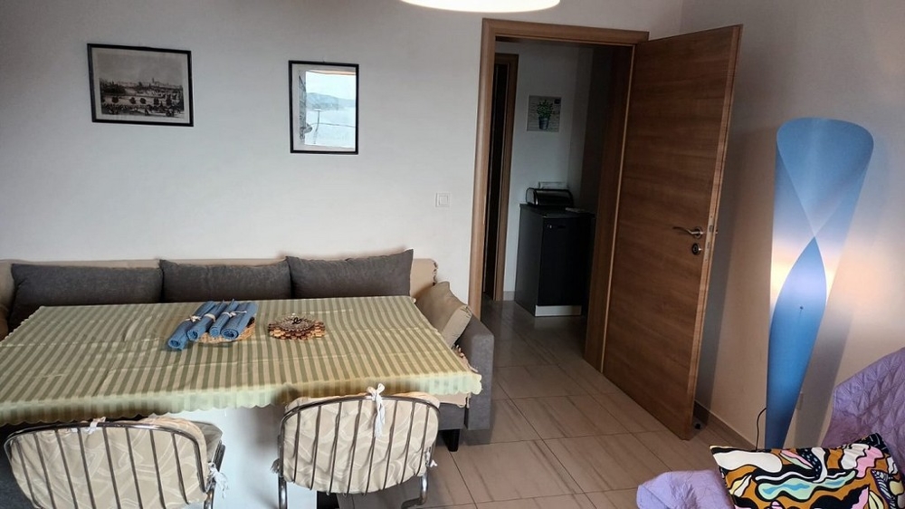 Jídelní kout s jídelním stolem a židlemi, vedle pohovky a otevřenými dveřmi do chodby.