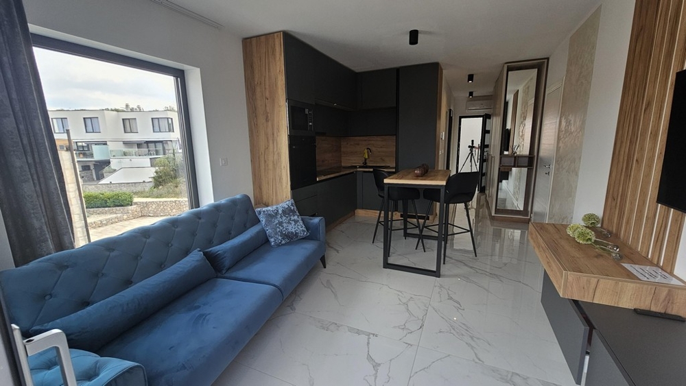 Obývací pokoj s pohovkou, přilehlá kuchyně a balkon