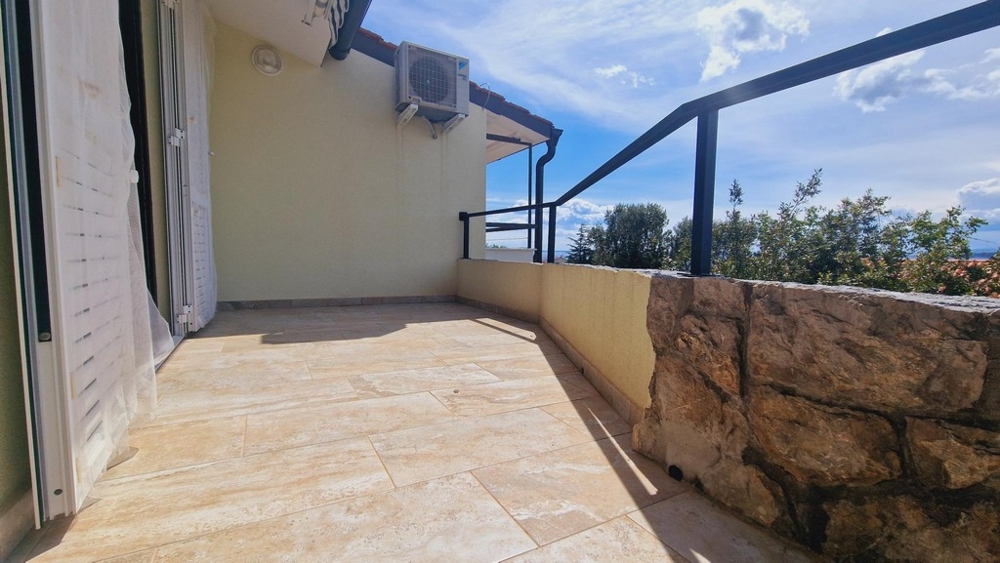 Slunná terasa s kamennou zdí a výhledem na okolní zeleň a oblohu.