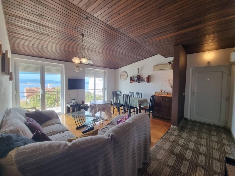Obývací pokoj se vstupem na balkon, dřevěný strop a výhled na moře.