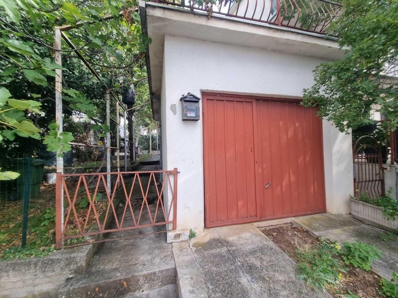 Garáž s červenými garážovými vraty a malou zahrádkou před domem.