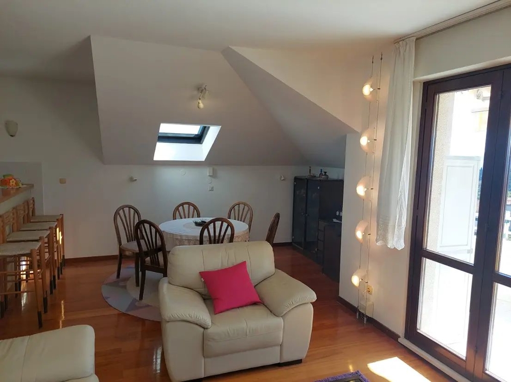 Jídelní stůl v podkrovním bytě, velká okna a barové židle u kuchyňské linky