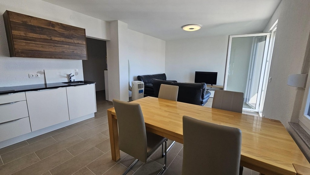 Moderní otevřená kuchyně s dřevěnými prvky, jídelním koutem a posezením vedoucím na balkon.