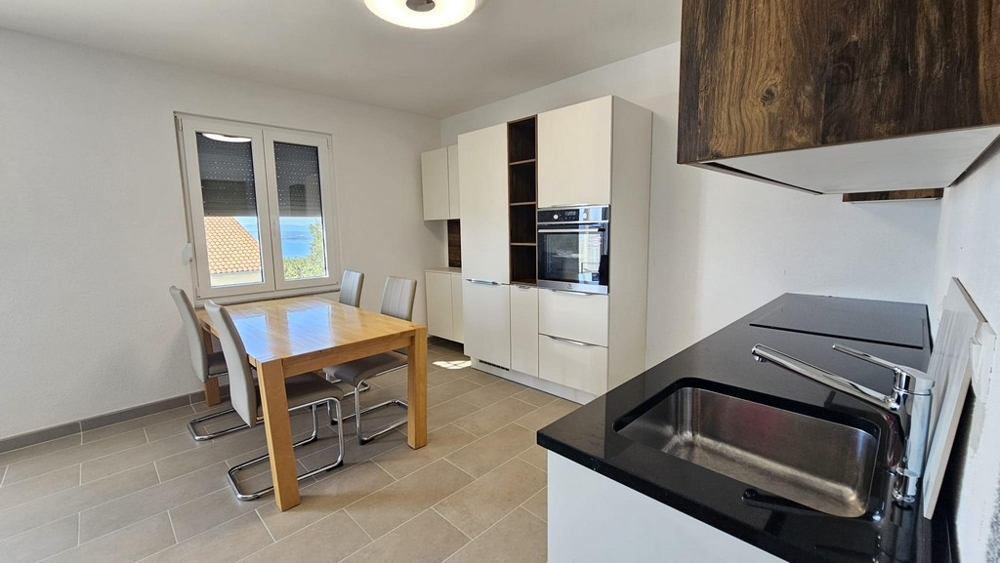 Světlá kuchyně s jídelním stolem, moderními spotřebiči a oknem s výhledem na moře.