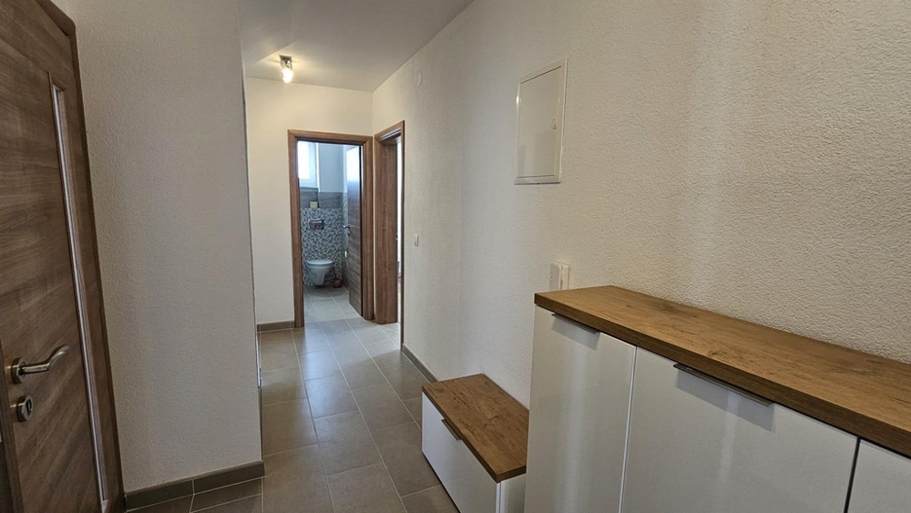 Předsíň vedoucí do koupelny s dlažbou a dřevěnými akcenty.