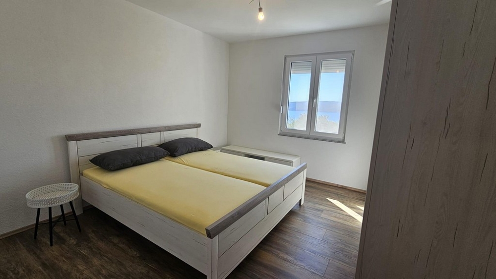 Ložnice s manželskou postelí a oknem s výhledem na moře.