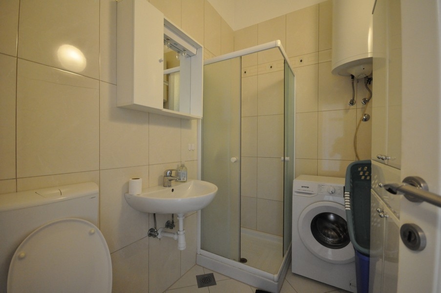 Koupelna se sprchovým koutem, umyvadlem, toaletou a pračkou, světlé obklady stěn a podlahy