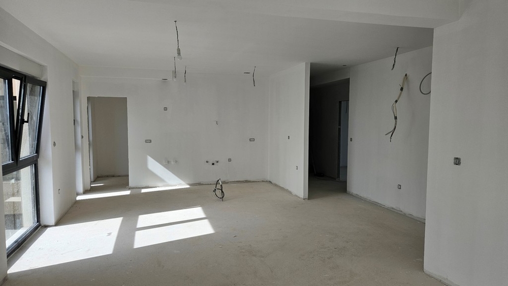 Nedokončený obývací prostor s otevřenými okny a připravenými přípojkami na kuchyň
