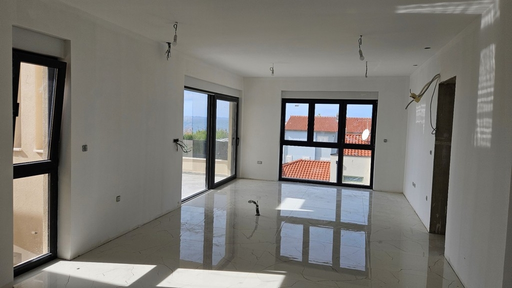 Obývací část s velkými okny a výhledem na červené střechy a balkon