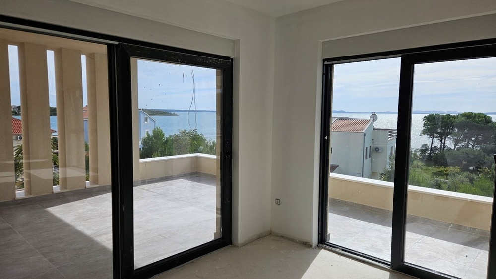 Obývací pokoj s velkými prosklenými okny s výhledem na moře a balkonem