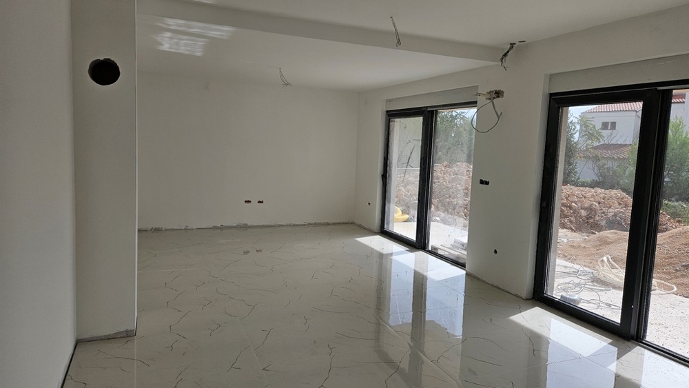 Interiér s velkou plochou oken, bílými stěnami a dlážděnou podlahou, stále ve výstavbě.