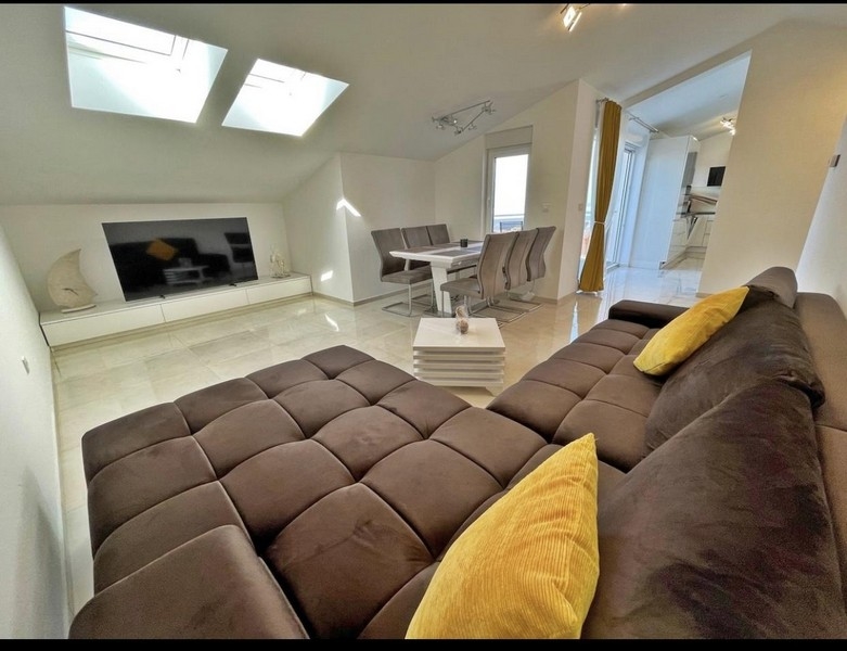 Moderní obývací pokoj se střešními okny, velkou pohovkou, jídelním stolem a televizí.