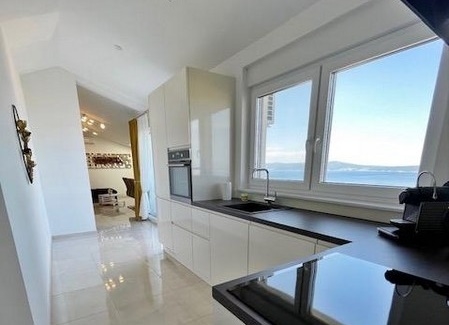 Kuchyně s bílými skříňkami, velkým oknem a výhledem na moře.